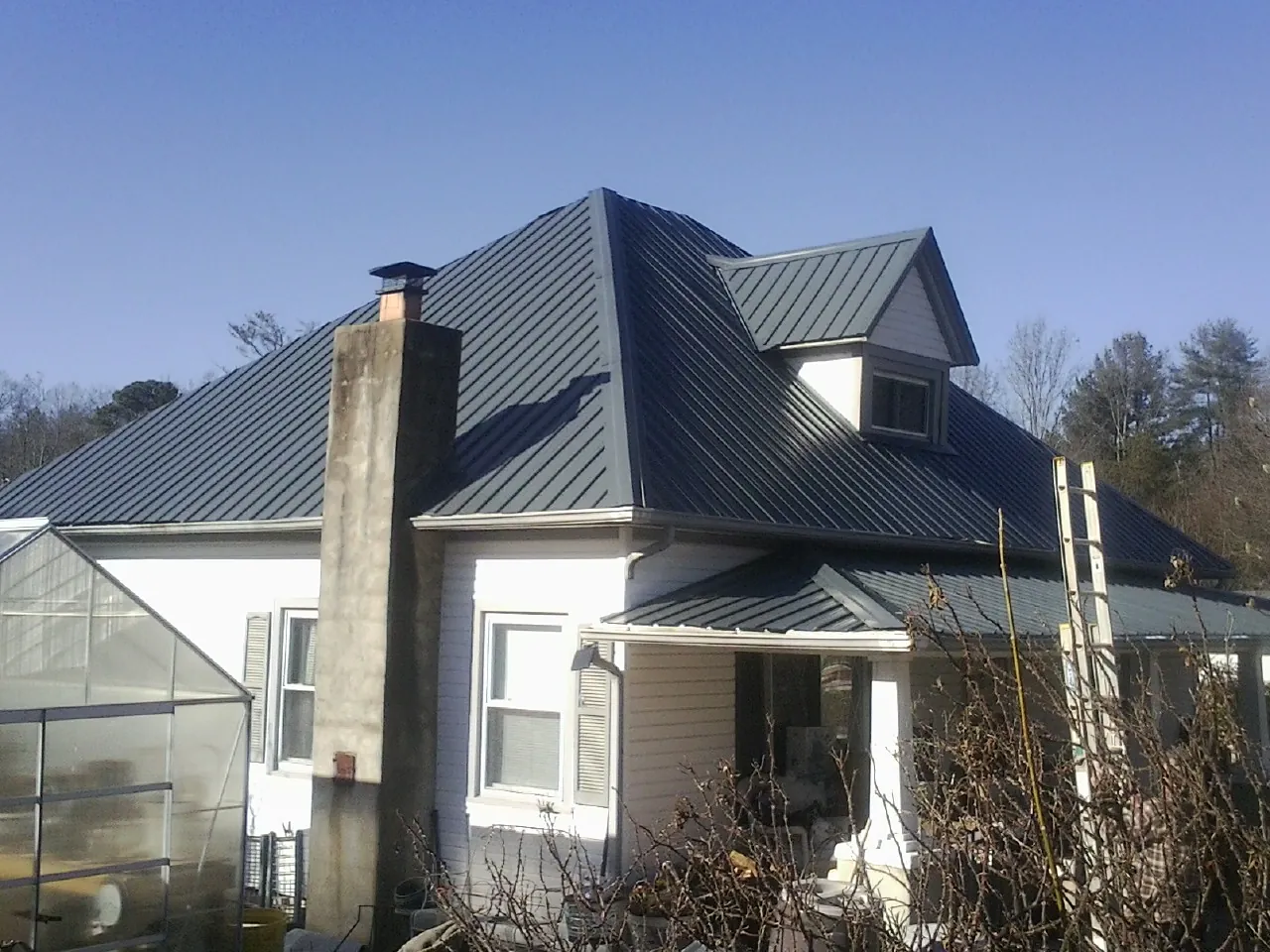 Dark blue standing seam metal roof on a white farmhouse with dormer — Slate & Tile Roof Repair by Roofing Brothers in Laura
