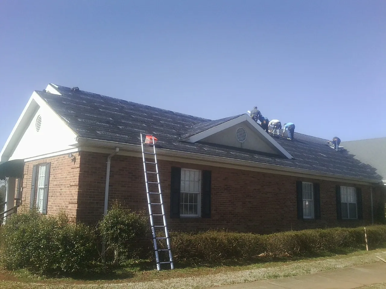 Crew tearing shingles off a brick ranch roof with a ladder set — Emergency Roof Repair work by our crew in Laura