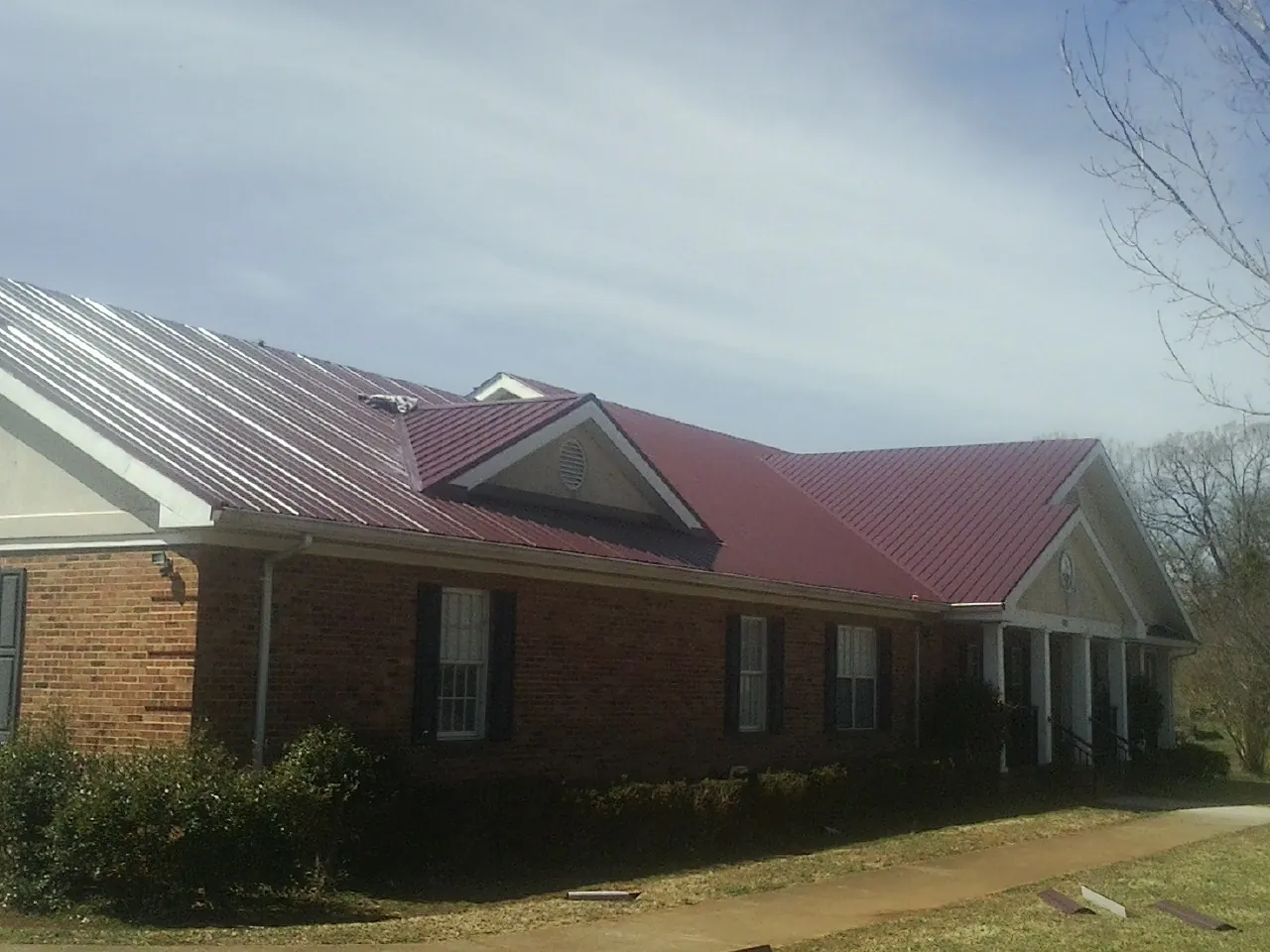 Red metal roof with gabled entries on a long brick building, from a Hail Damage Roof Repair job in Laura