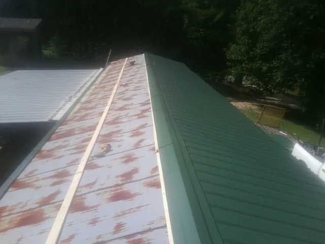 Old rusted panels beside newly installed green metal roofing — Wind Damage Roof Repair by Roofing Brothers in Laura