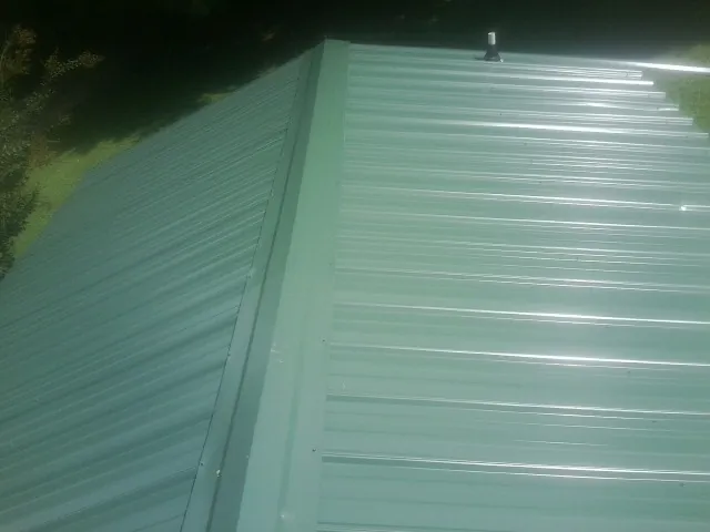 New green metal panels meeting at the ridge of a roof — Flat Roof Repair work by our crew in Laura