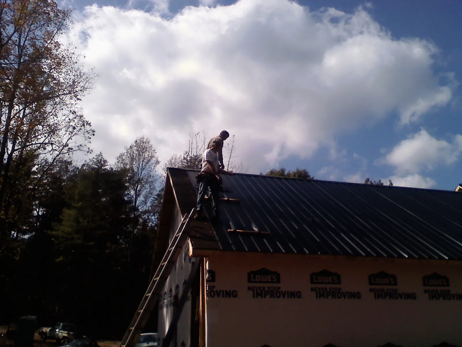 Roofer fastening dark metal panels high against a cloudy sky, from a Roof Inspection job in Laura