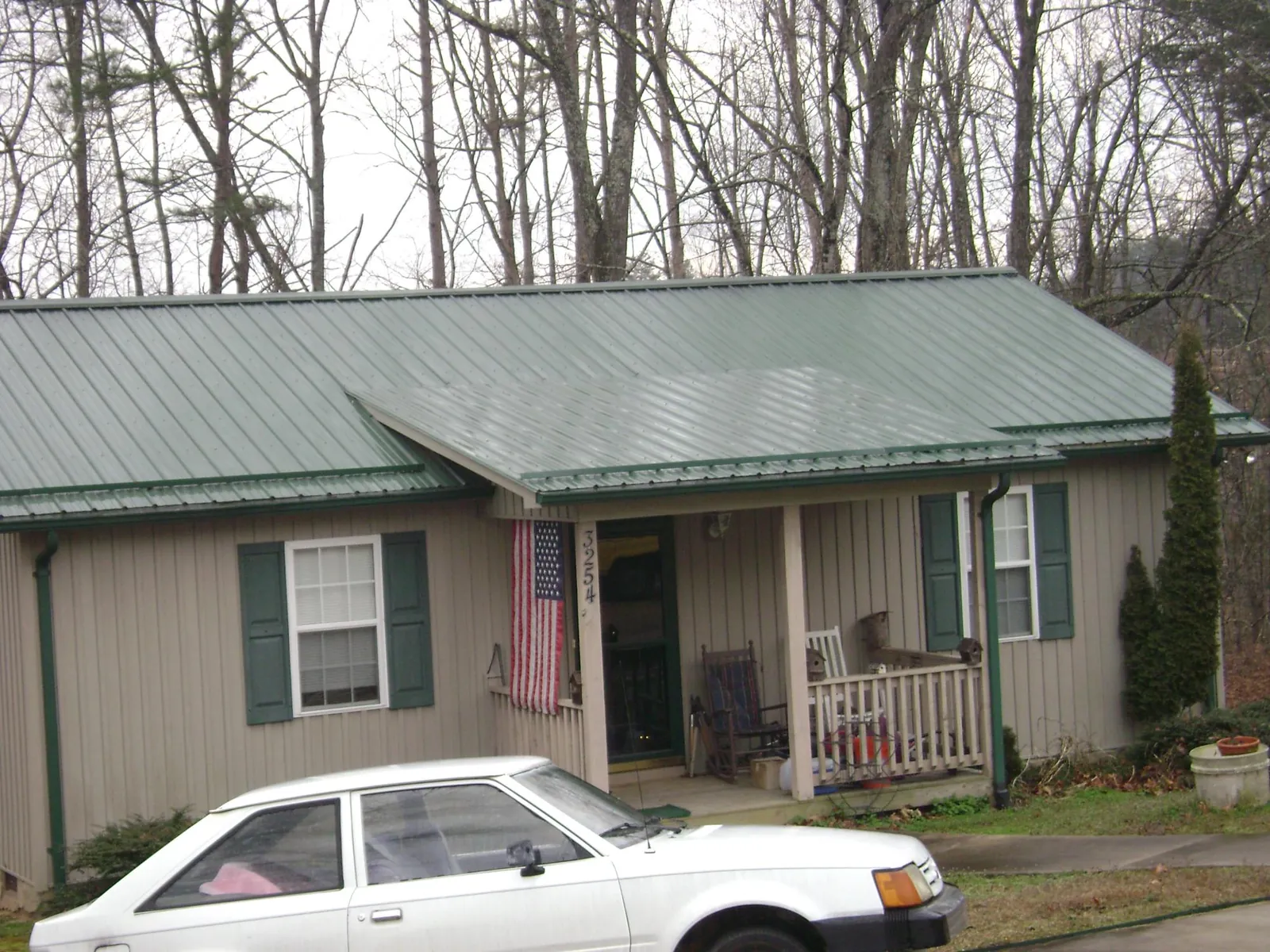 Green metal roof and front porch on a tan sided cottage in Laura
