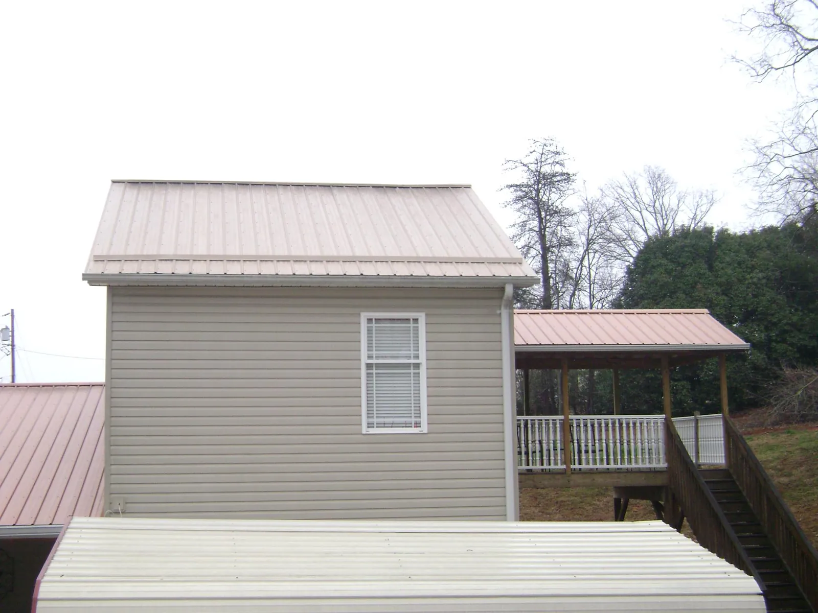 Tan metal roofs on a two story addition and attached porch, from a Roof Replacement job in Laura